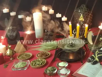 Tavolo rituale con candele, erbe e incensi su un telo rosso