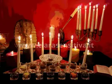 Tavolo rituale con candele bianche e rosse su fondo rosso scuro