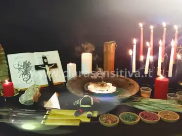 Tavolo rituale con candele, un libro aperto e ciotole di erbe